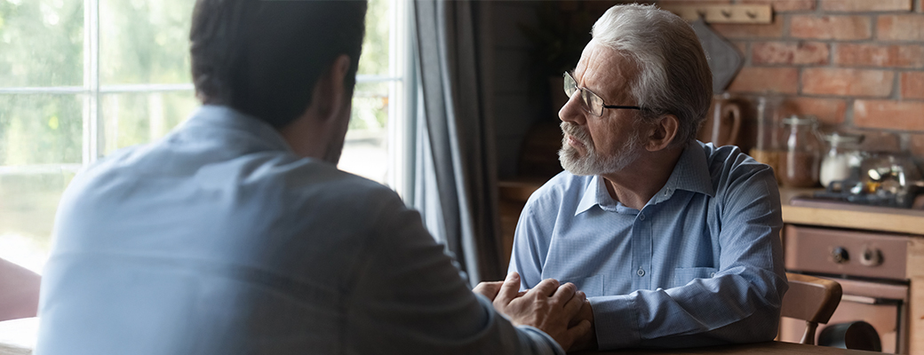 Image of senior male and middle aged male speaking at kitchen table